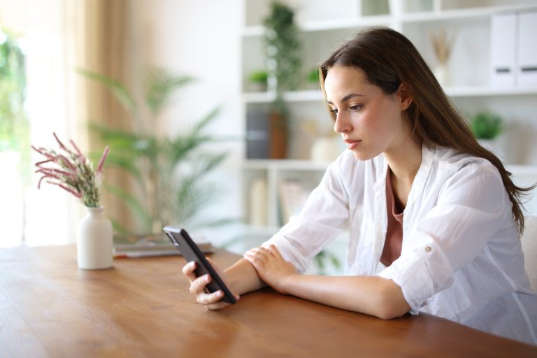 Serious,Woman,Checking,Mobile,Phone,Content,On,A,Table,At